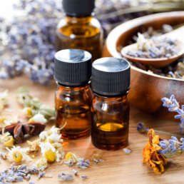 Amber essential oil bottles with black caps on a wooden surface amid dried lavender and botanicals (close-up)