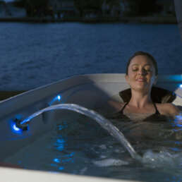 Woman relaxing in a blue-lit hot tub at night with eyes closed by the water surface.