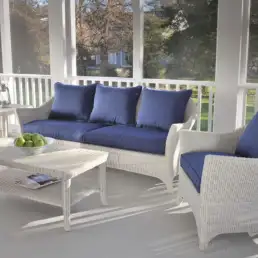 White wicker patio furniture with blue cushions on a sunlit screened porch; coffee table with a bowl of green apples.