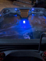Outdoor hot tub at night with blue LED lights and swirling water shapes the scene.